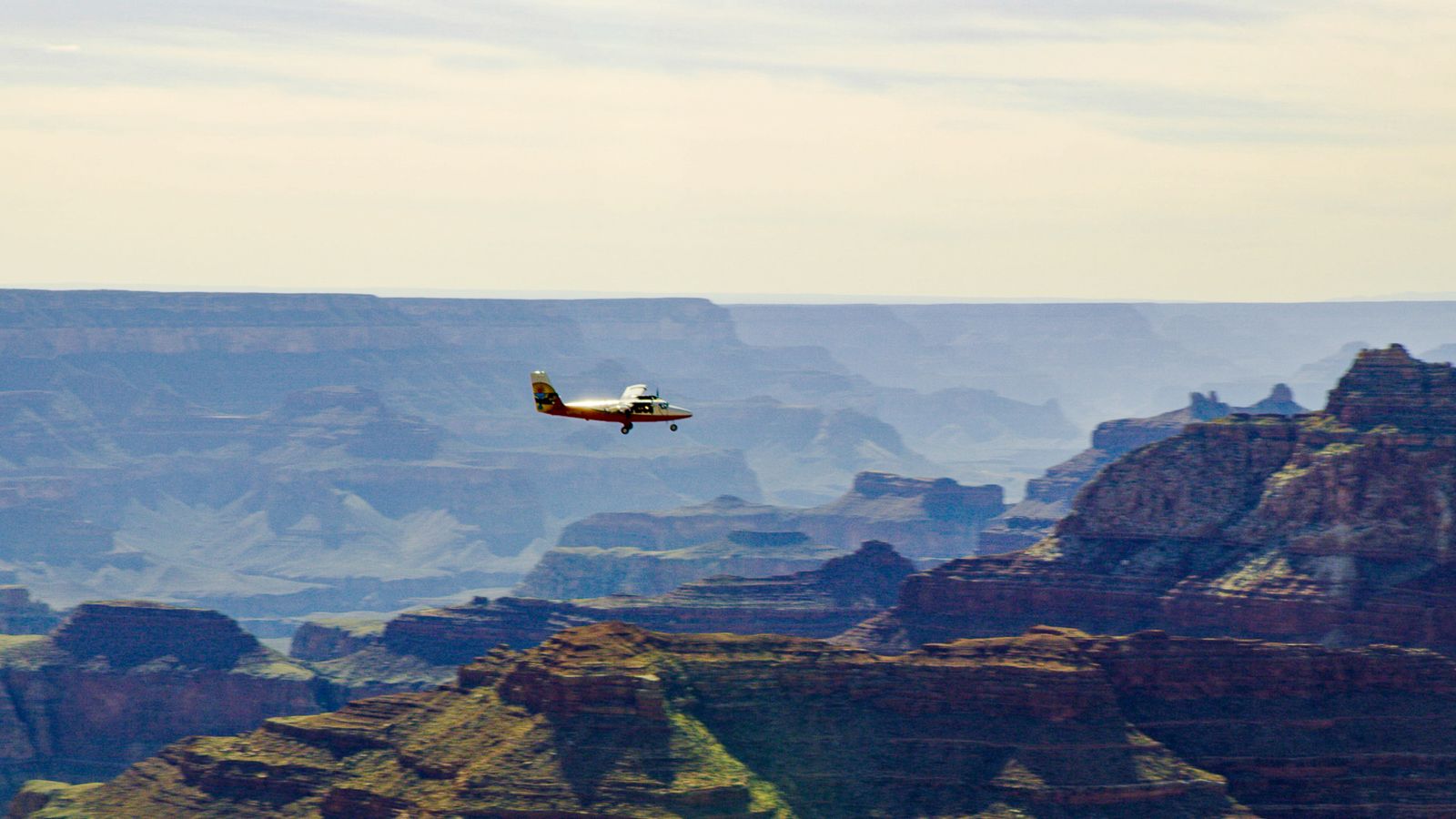 A touring airplane soars over the South Rim landscape with the canyon walls in the distance