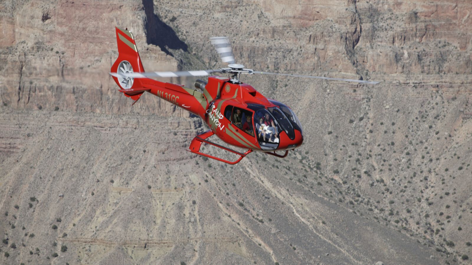 Red EC130 flying over the east rim of the Grand Canyon