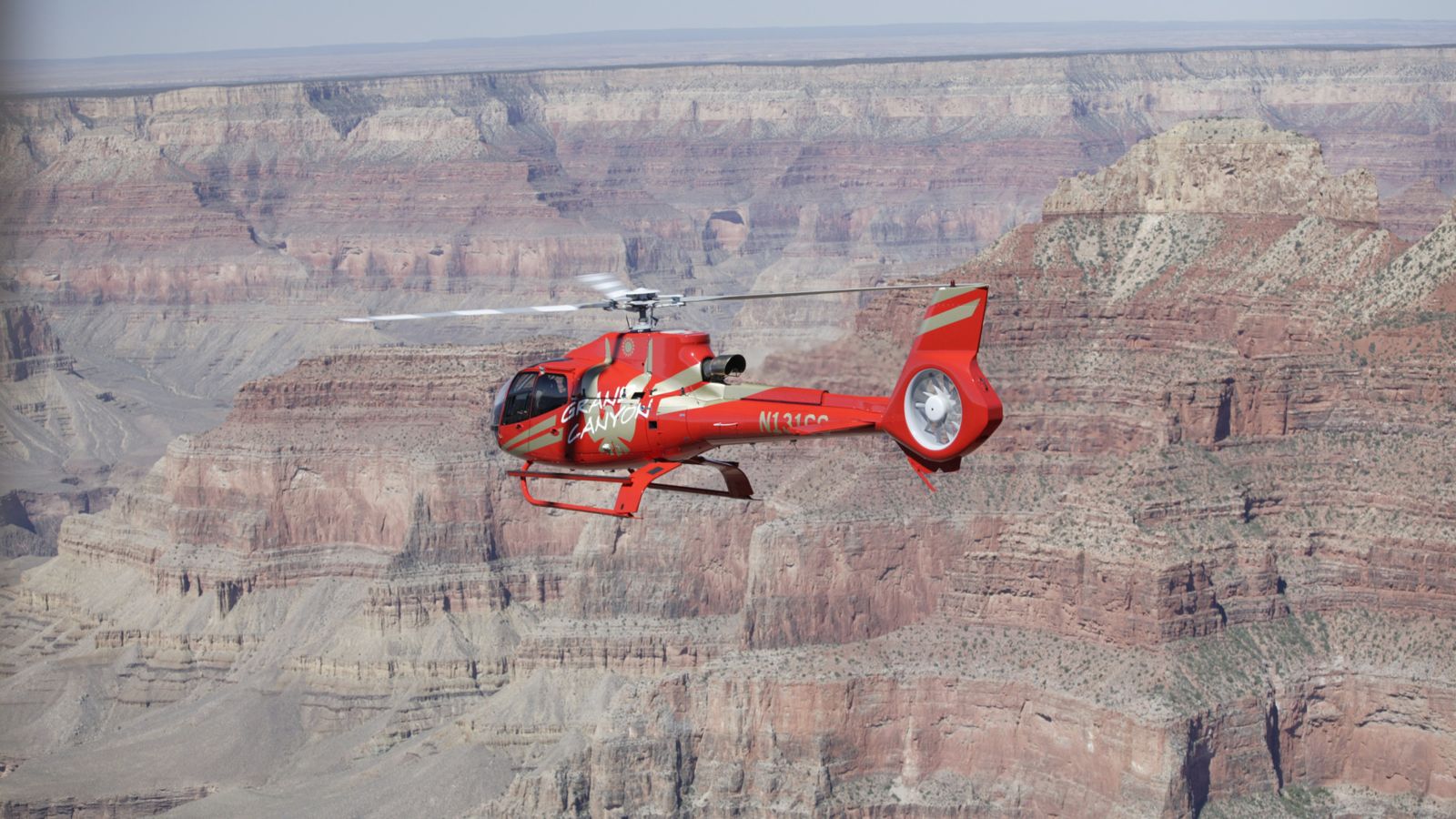 A red EcoStar helicopter flies through the Grand Canyon National Park stone walls