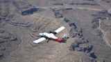 A red and white airplane mid-flight on a Grand Canyon tour, seen from above.