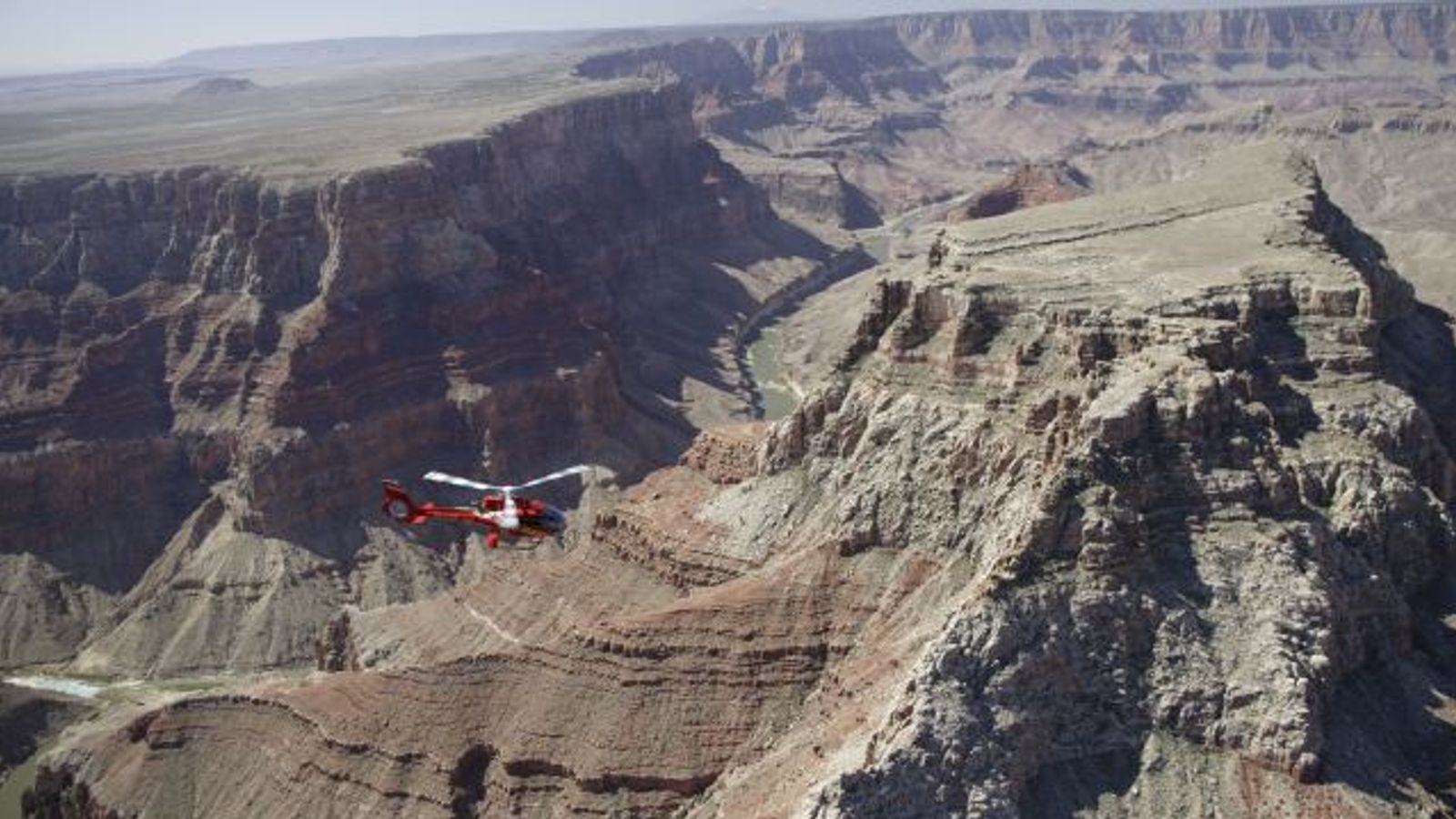 a large swathe of the grand canyon national park landscape with a helicopter tour seen in the distance
