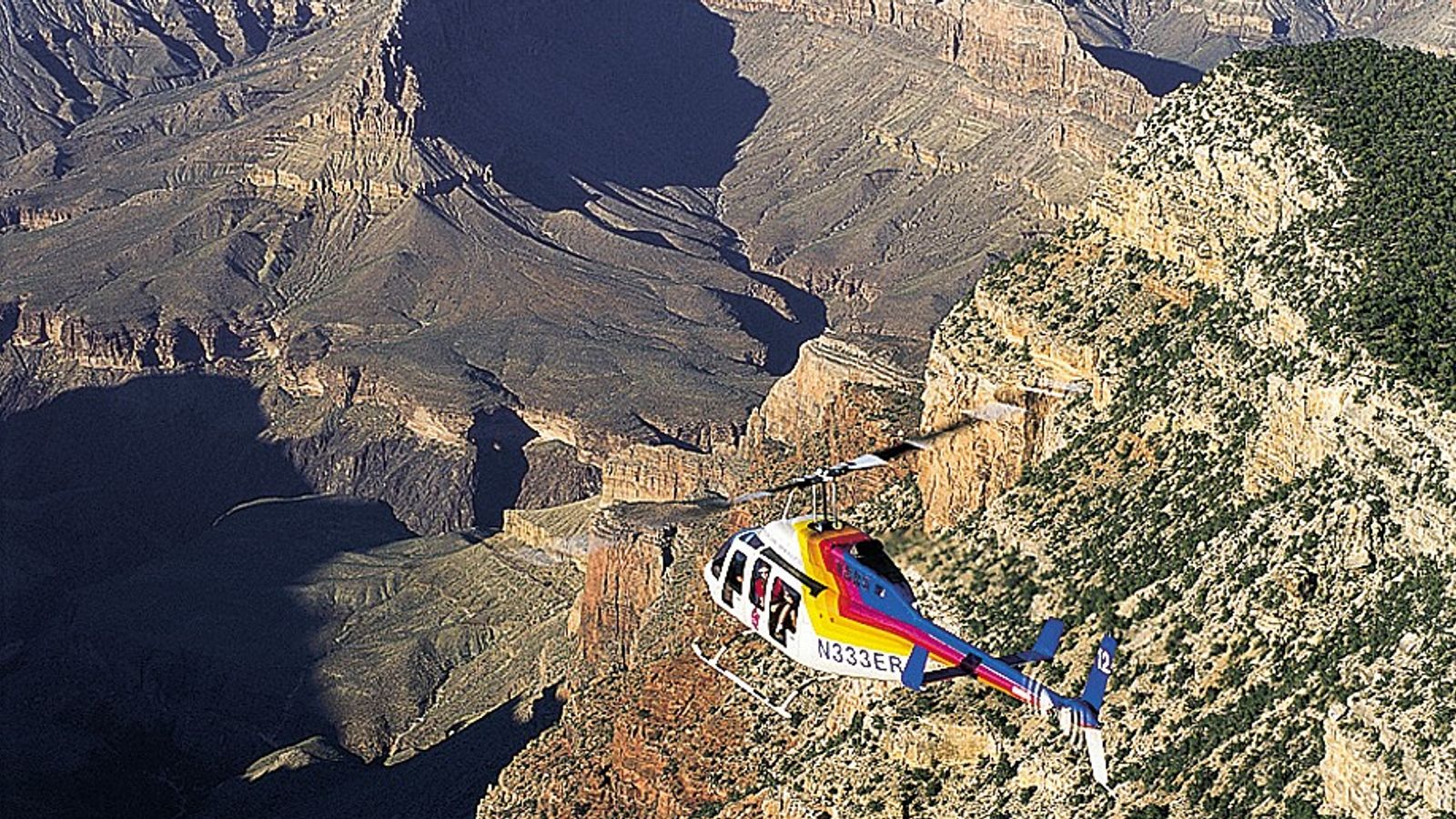 A Bell Tour Helicopter as it flys over the eastern rim of Grand Canyon and out into the vast expanse.