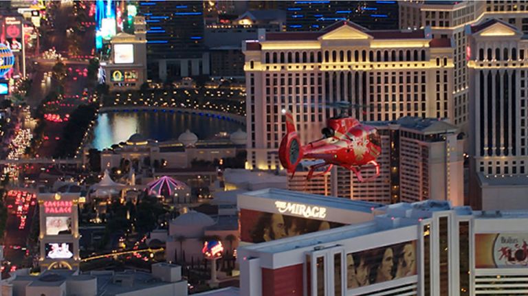 a red helicopter flies over the brightly lit las vegas casinos at night