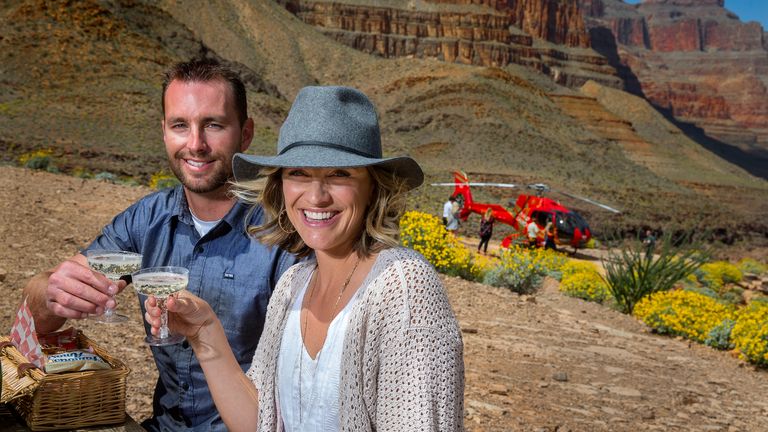 a couple poses with champagne on the floor of the Grand Canyon during a helicopter tour from Las Vegas