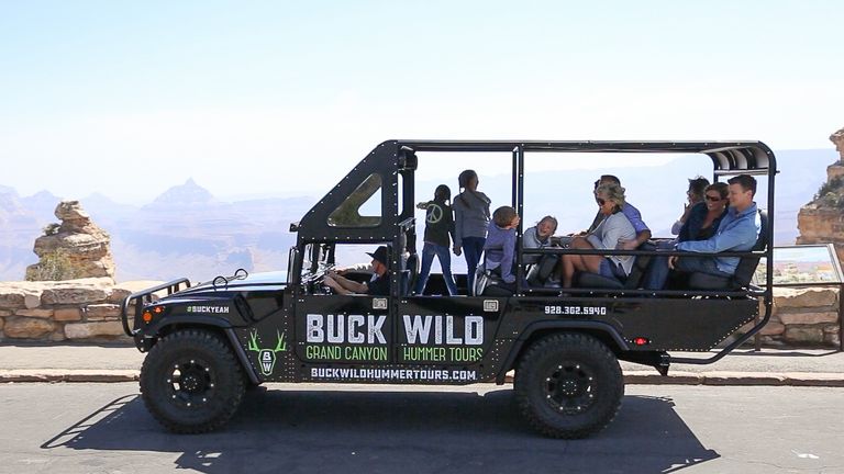 passengers sit in an open-air Hummer vehicle parked at a Grand Canyon lookout point