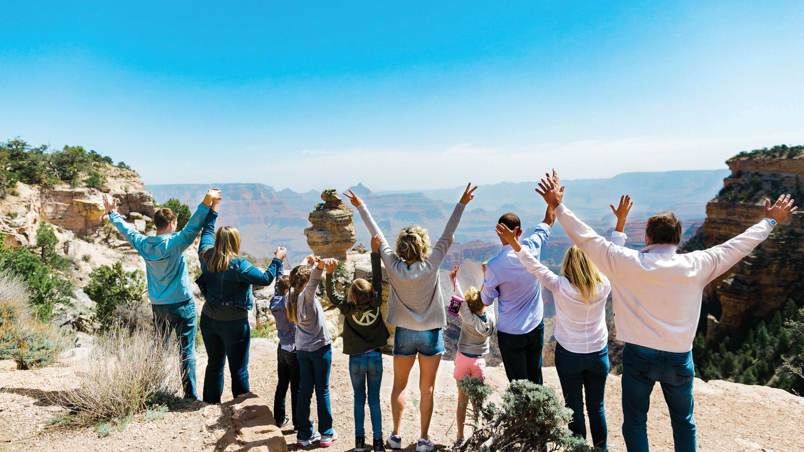 Guests with their arms raised standing near the edge of the Grand Canyon.