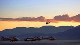 Several helicopters landed at an air terminal, with a backdrop of mountains at sunset.