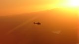 A helicopter flies in an orange sky at sunset.