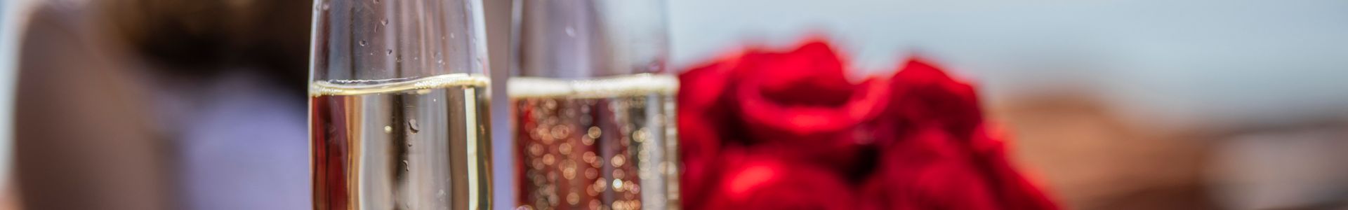 a closeup shot of champagne glasses with roses in the background