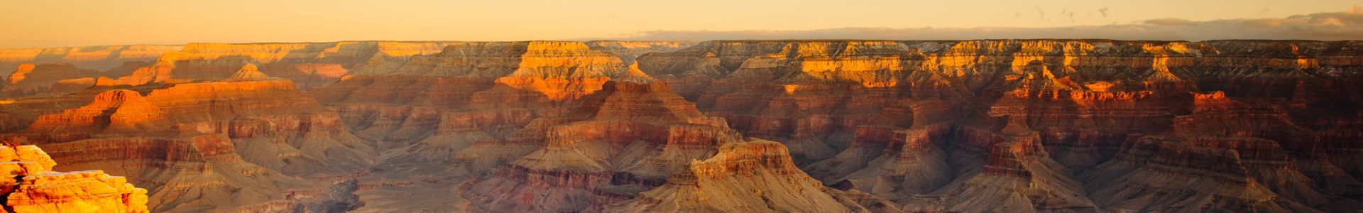 A golden sunset casts light across a vast wall of the Grand Canyon