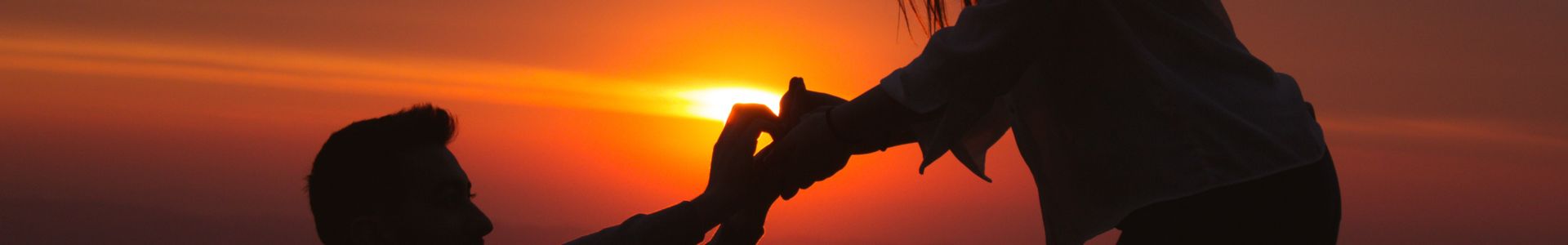 a silhouette of a man proposing to a woman in front of a bright orange sunset