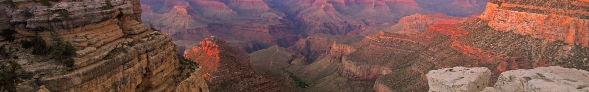 The Grand Canyon National Park with pink light from the sunset scattered across the stone walls.
