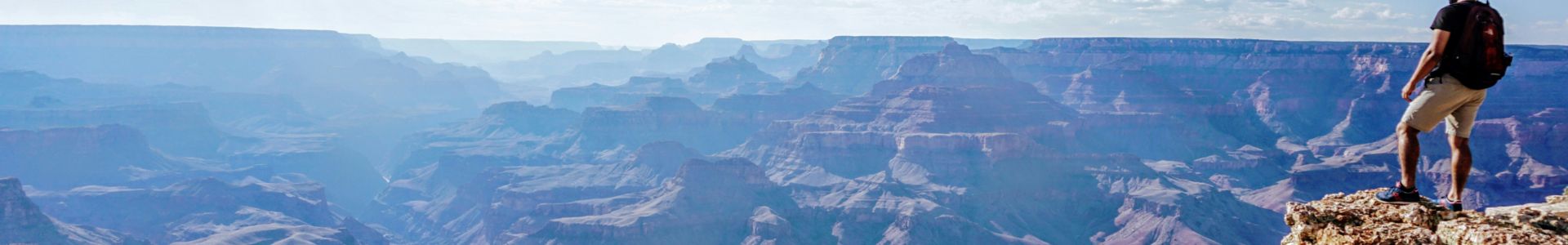 a man stands atop a lookout point in front of a stunning Grand Canyon landscape