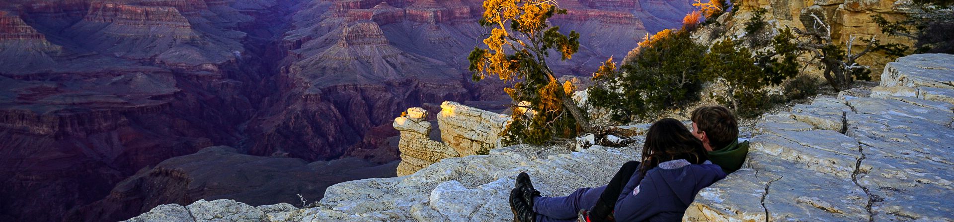A couple sits at the edge of a Grand Canyon lookout point at sunset