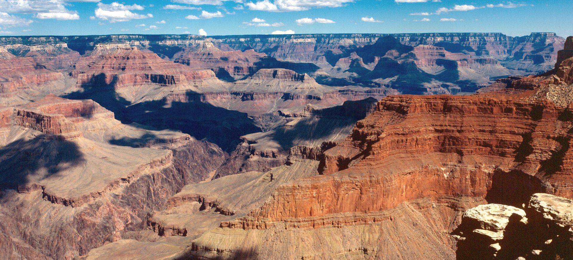 The colorful striped walls of the Grand Canyon South Rim seen beneath blue skies and clouds