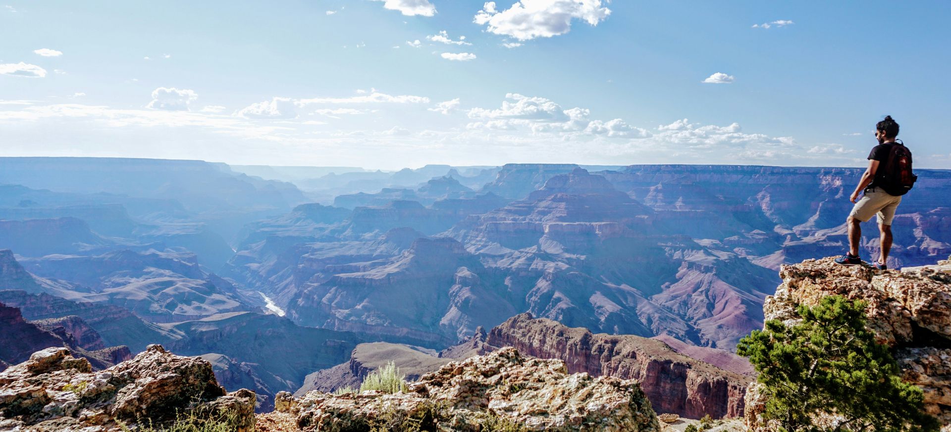 a man stands atop a lookout point in front of a stunning Grand Canyon landscape