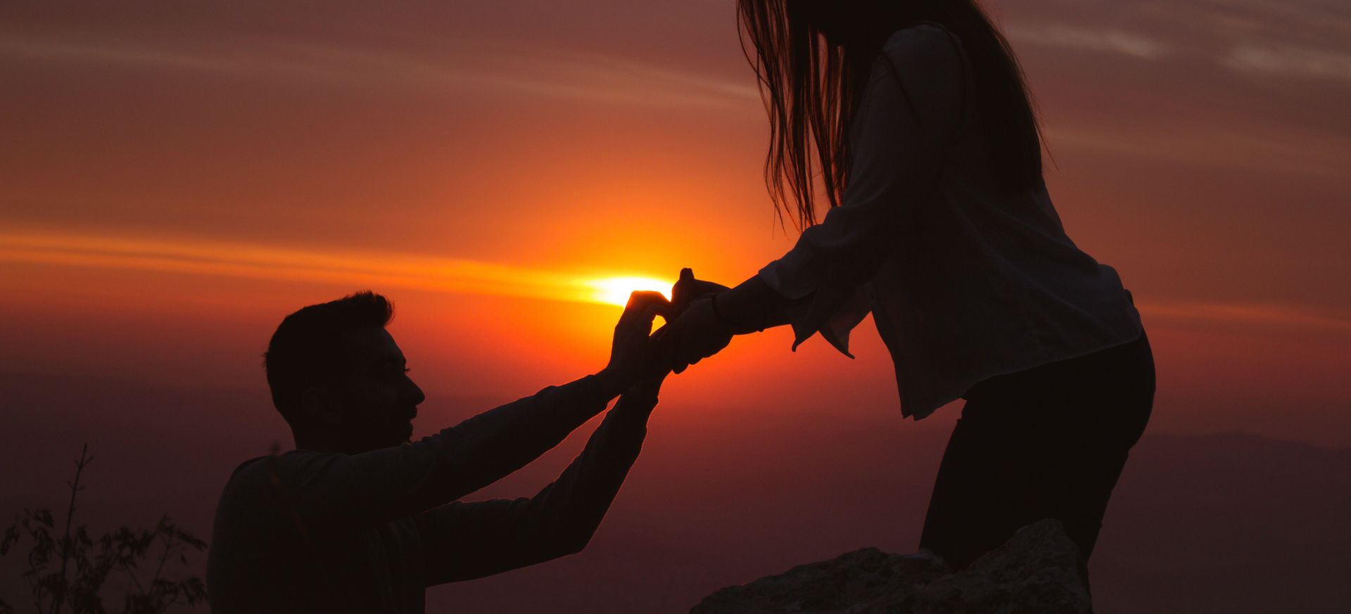a silhouette of a man proposing to a woman in front of a bright orange sunset