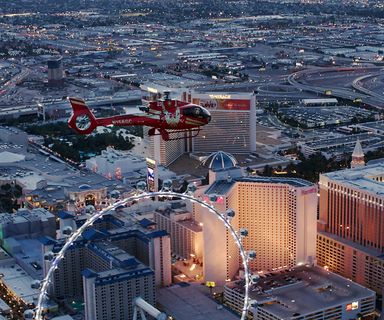 A red helicopter flies over the Las Vegas Strip and High Roller Observation Wheel.