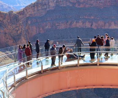 several guests stand and sit atop the Skywalk glass bridge at Grand Canyon West