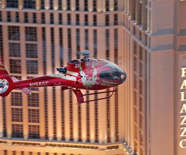 Red helicopter flying over Las Vegas past the Palazzo Hotel at night