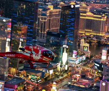 a red helicopter flies over the lit-up Strip casinos at night during a Las Vegas helicopter tour