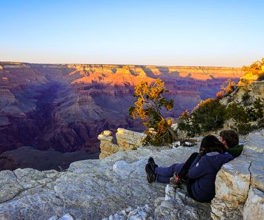 A couple sits at the edge of a Grand Canyon lookout point at sunset