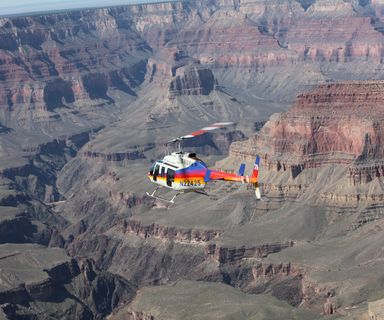 A rainbow helicopter flies over the Grand Canyon and Colorado River.