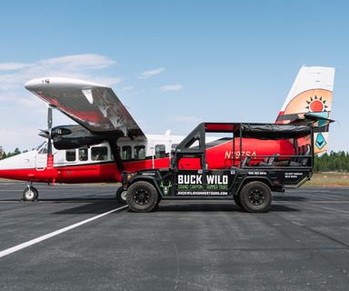 A side view of a Twin Otter airplane parked next to a Hummer vehicle