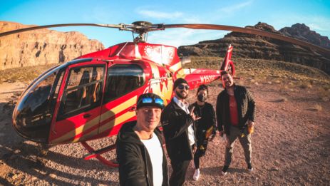 a group of men pose for a selfie in front of a helicopter at the bottom of the Grand Canyon West