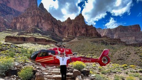 a helicopter tour pilot poses with his helicopter at the bottom of the grand canyon