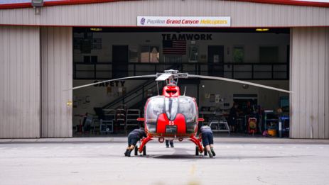 two mechanics push a papillon helicopter into a hangar for routine maintenance