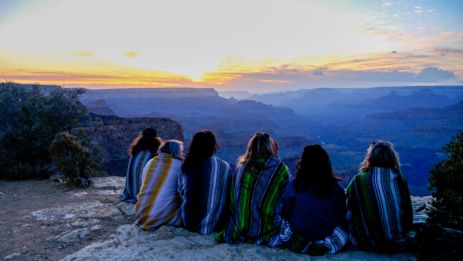 a group of people sit at the edge of the Grand Canyon National Park during sunset
