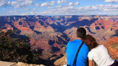 a couple sits facing an expansive Grand Canyon landscape