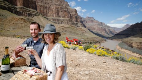 a couple smile while sitting at a picnic table after landing on the bottom of the Grand Canyon West