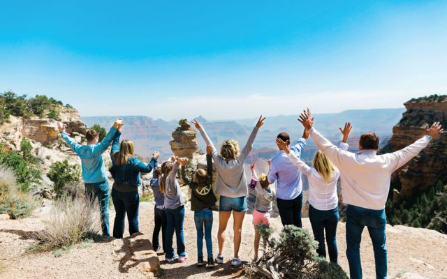 a family stands at a Grand Canyon National Park viewpoint with their arms in the air