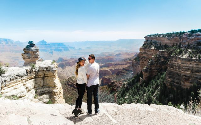 a male and female couple stand at a Grand Canyon lookout point turning toward the camera