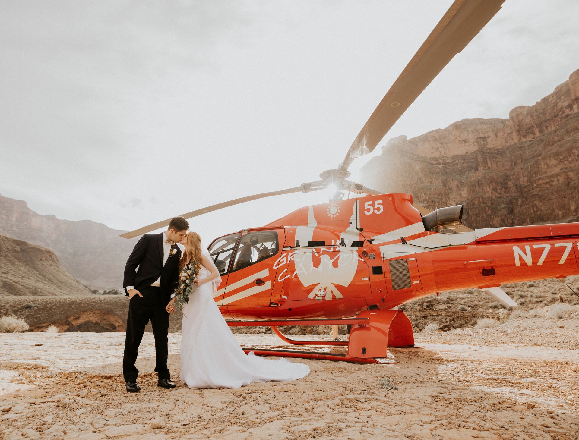 Groom kissing bride next to red helicopter at the bottom of Grand Canyon West, Las Vegas wedding package all-inclusive.