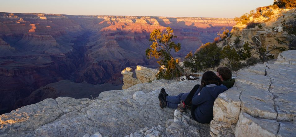 a couple sits at the edge of the Grand Canyon watching the sunset