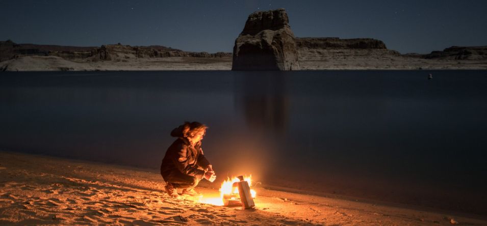 person sitting in front of a campfire at lone rock beach in page arizona