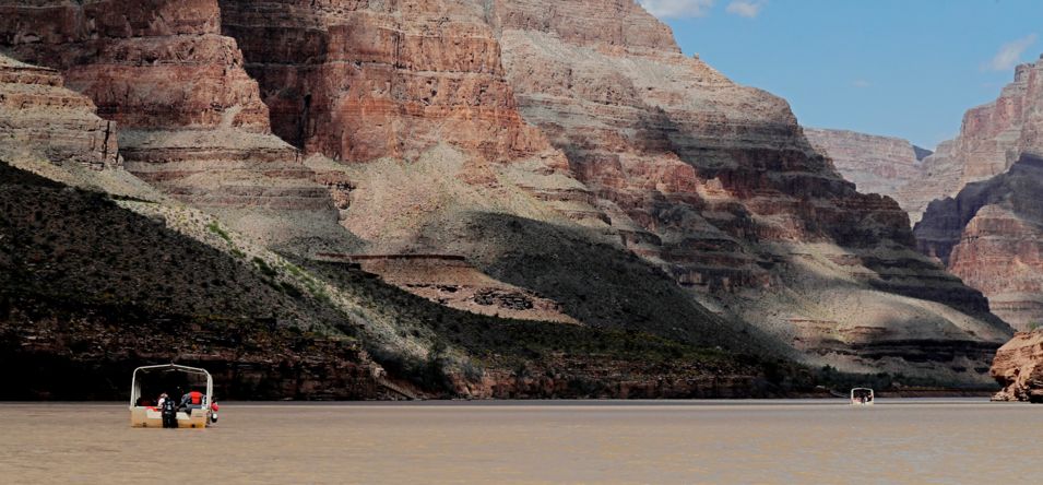a pontoon boat floating down the Colorado River between the walls of the Grand Canyon West