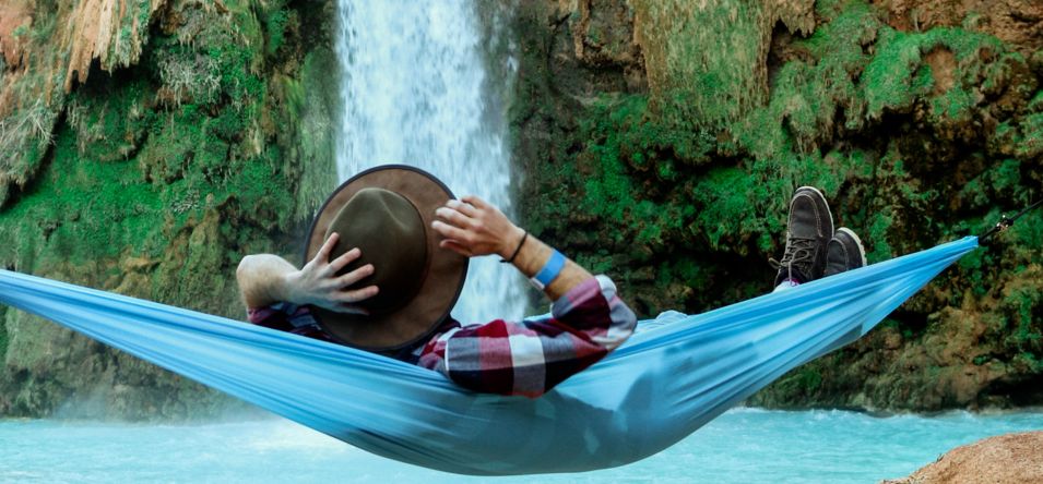 A man rests in a hammock while watching a waterfall within Havasu Falls