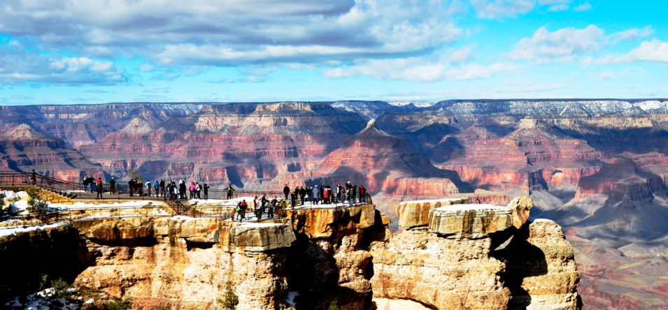 several visitors stand on the very edge of a Grand Canyon National Park lookout point
