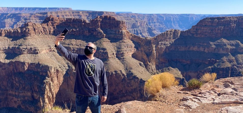 a man stands at the edge of the Grand Canyon West and takes a selfie with the canyon gorge behind him