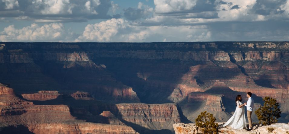 a man and woman stand holding hands at the edge of a Grand Canyon lookout point