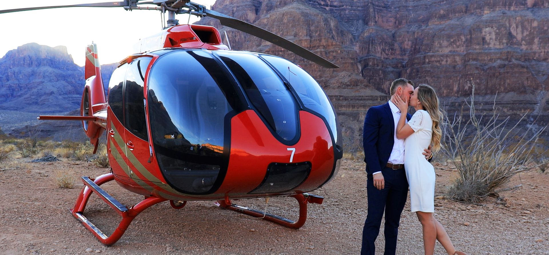 a couple kisses in front of a helicopter landed on the bottom of the Grand Canyon West