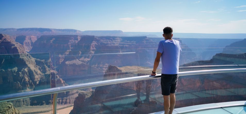 a man stands atop the Skywalk Bridge in front of expansive Grand Canyon West scenery