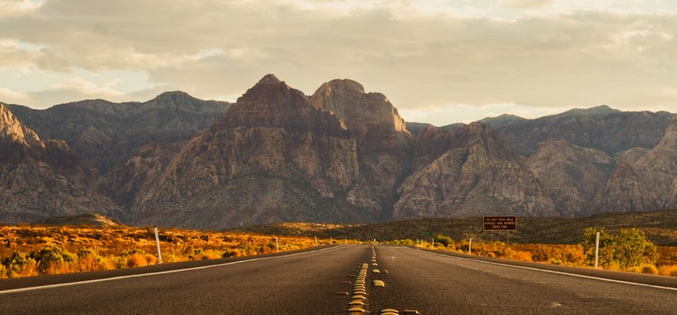a section of the Red Rock Canyon Scenic Drive at sunset with massive canyon walls in the distance