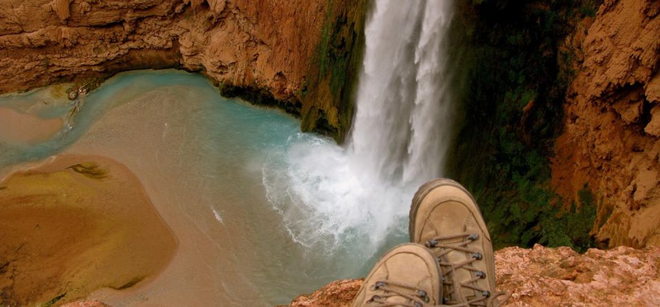 a closeup of the boots of a Havasu Falls visitor resting on the edge of a canyon overlooking a waterfall