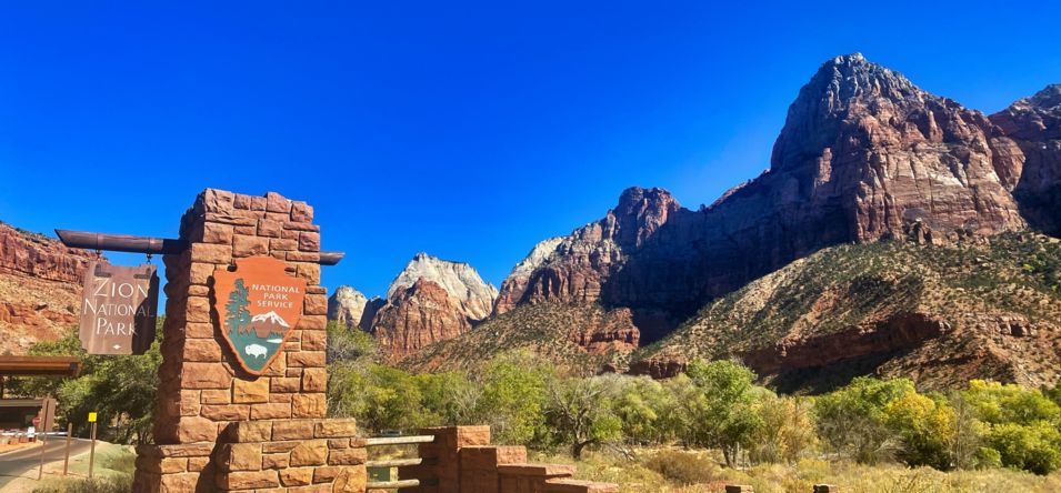 the entrance sign outside Zion National Park with the massive canyon walls in the background