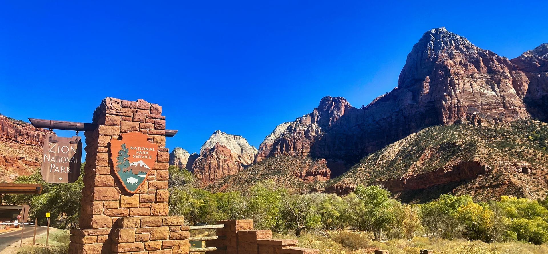 The entrance sign outside Zion National Park with the massive canyon walls in the background